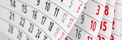 Curved pages of a calendar showing a month with numbers in black and Sundays in red.