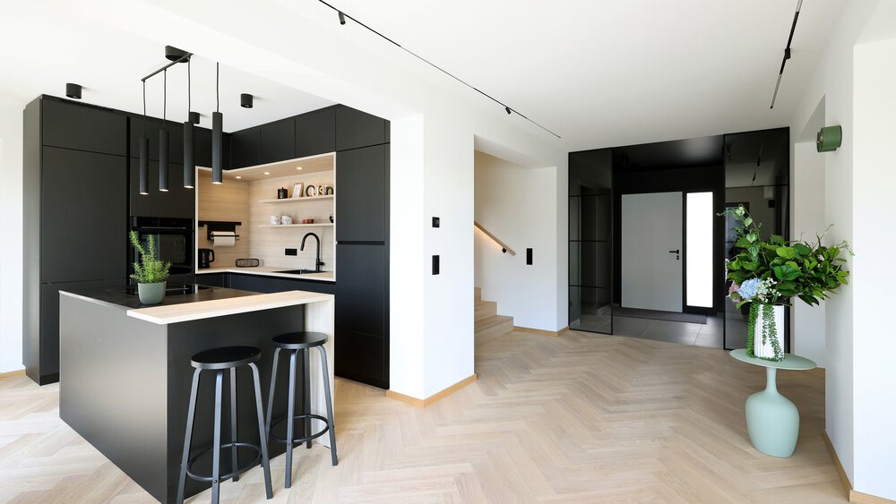 Moderne Küche mit schwarzen Schränken, Kochinsel mit Hockern und einer Blumenvase in einem hellen, offenen Raum.