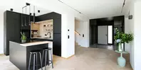 Moderne Küche mit schwarzen Schränken, Kochinsel mit Hockern und einer Blumenvase in einem hellen, offenen Raum.