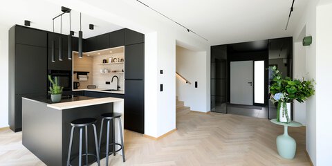 Moderne Küche mit schwarzen Schränken, Kochinsel mit Hockern und einer Blumenvase in einem hellen, offenen Raum.