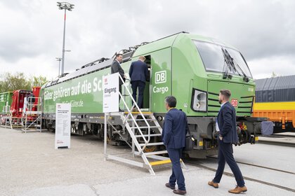 Ein grüner Waggon der DB Cargo steht auf dem Freigelände der Messe München. Vier Männer in Anzügen betreten den Zug über eine weiße Metalltreppe.