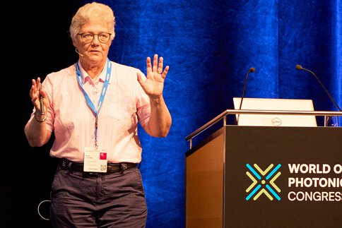 Person steht auf der Bühne des World of Photonics Congress und spricht neben einem Rednerpult mit aufgeklapptem Laptop.