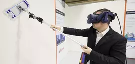 A man in a suit wears a headset and wipes the wall of a stand at productronica with a mop.