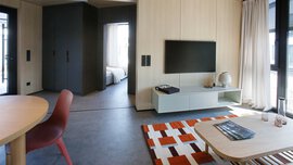 Modernes Wohnzimmer mit Fernseher, Teppich, Couchtisch und Blick in ein Schlafzimmer; minimalistische Einrichtung.