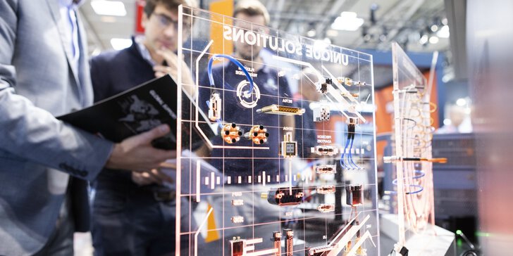 Two people examining a transparent board with technical circuit diagrams and electronic components indoors