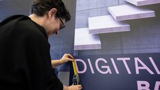 Ein misst mit einem Maßband die Länge eines Buchstabens auf einem Plakat