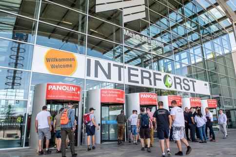 Personen betreten die INTERFORST-Ausstellung auf der Messe München durch mehrere Drehtüren, darüber sind das Messe- und INTERFORST-Logo zu sehen.
