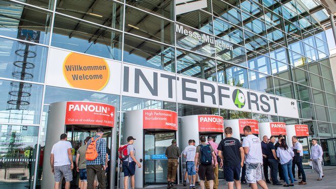 People enter the INTERFORST exhibition at Messe München through several revolving doors, above which the trade fair and INTERFORST logos can be seen.