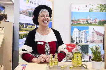 Exhibitor in traditional attire cheerfully presents Upper Bavaria's travel highlights.