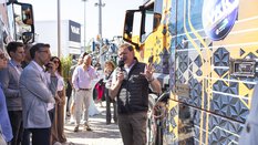 Mann, der bei einer Live Demonstration im Freien neben einem bunt bedruckten Lastwagen zu einer Gruppe Besucher spricht.
