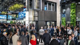 Eine große Menschenmenge versammelt sich in einer Innenausstellung mit moderner Architektur und grünen Wänden.