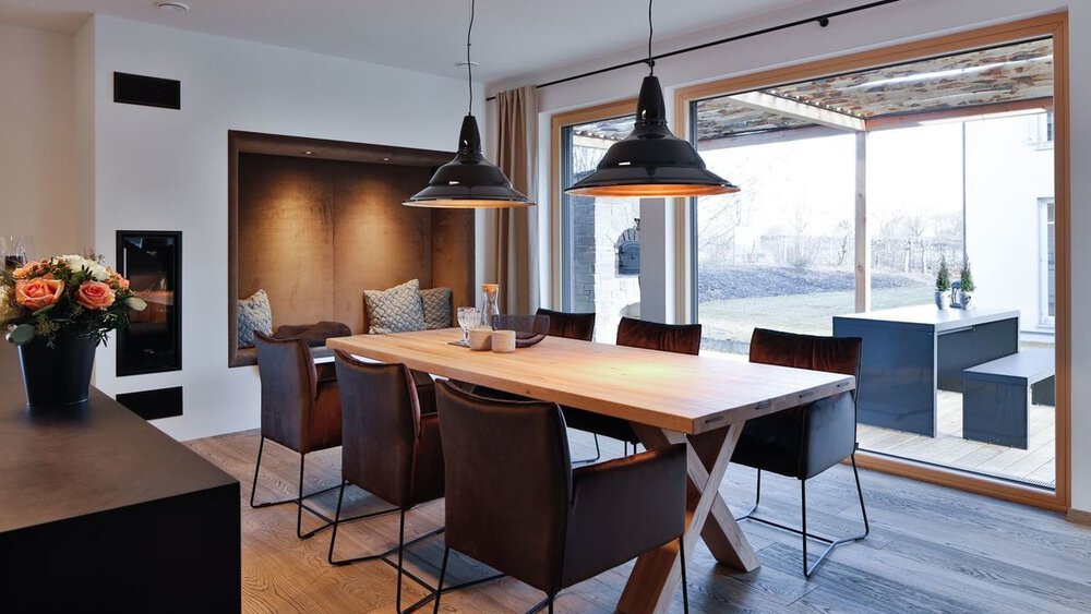 Moderner Essbereich mit Holztisch, sechs Stühlen, Pendelleuchten, Wandbank und großem Fensterblick.