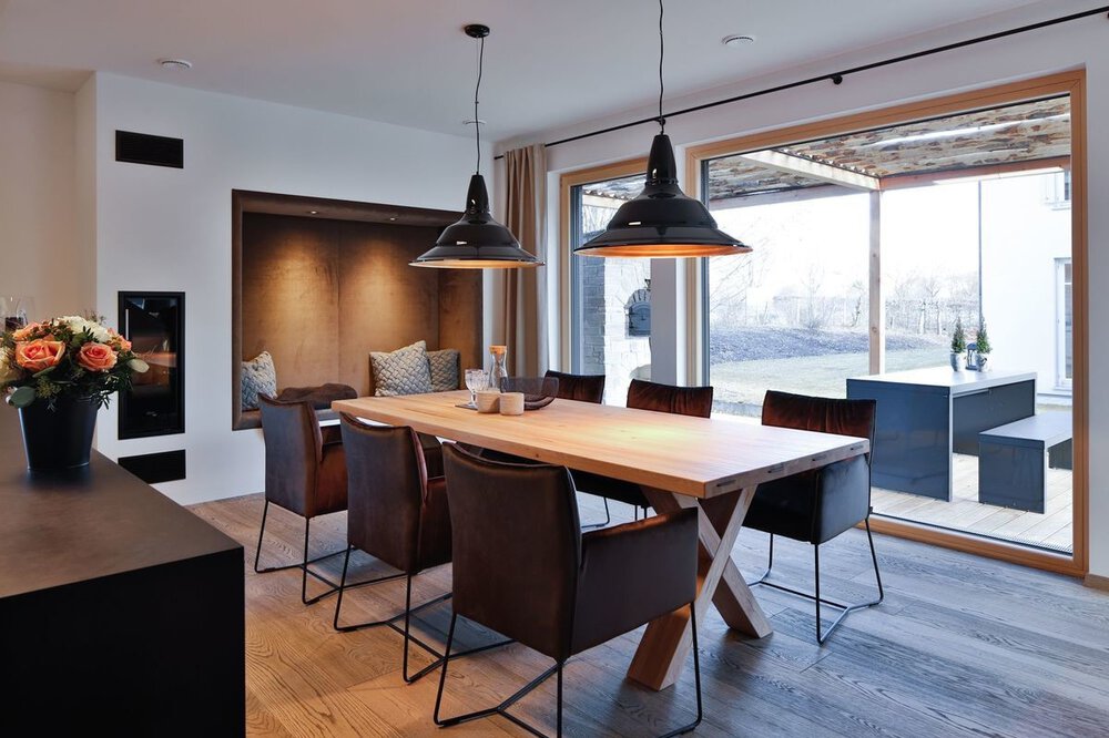 Moderner Essbereich mit Holztisch, sechs Stühlen, Pendelleuchten, Wandbank und großem Fensterblick.