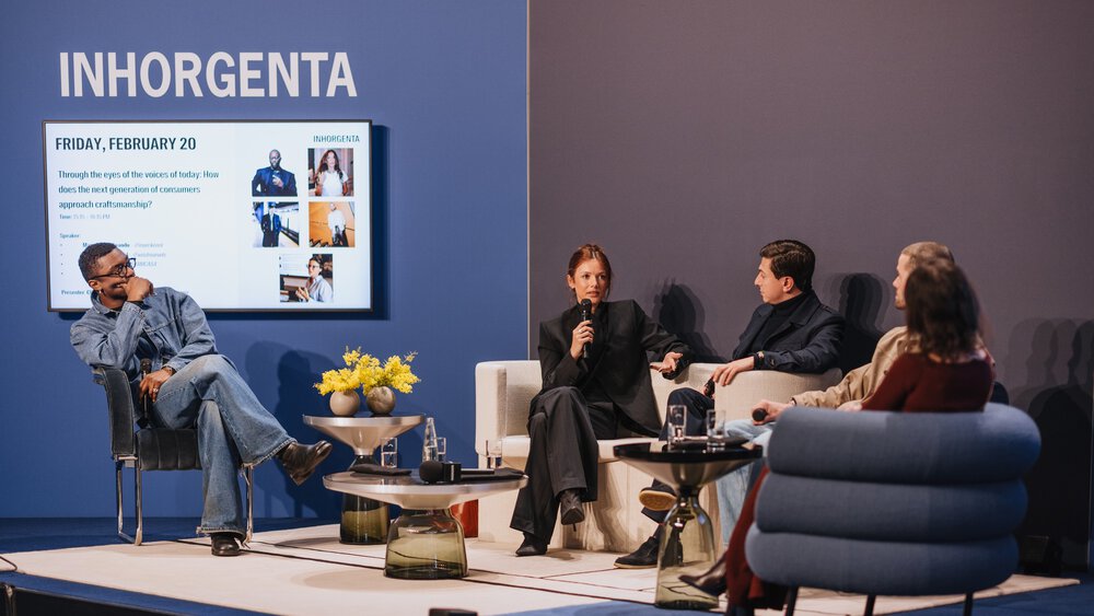 Vier Personen sitzen auf einer Inhorgenta-Veranstaltung auf der Bühne und diskutieren, während hinter ihnen ein Bildschirm mit Veranstaltungsdetails angezeigt wird.