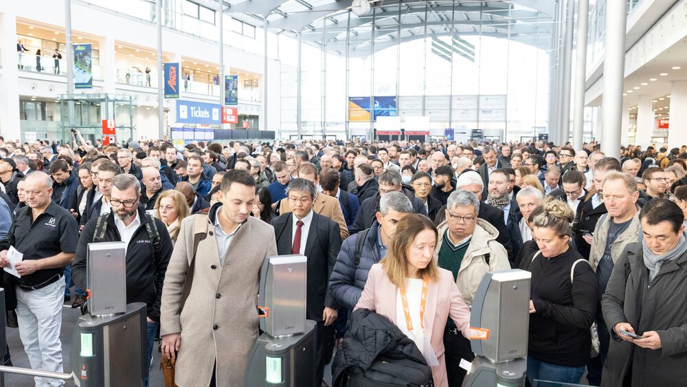 Numerous visitors stand in the entrance hall of the Munich Exhibition Centre, waiting to be admitted to the productronica trade fair.