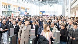 Numerous visitors stand in the entrance hall of the Munich Exhibition Centre, waiting to be admitted to the productronica trade fair.