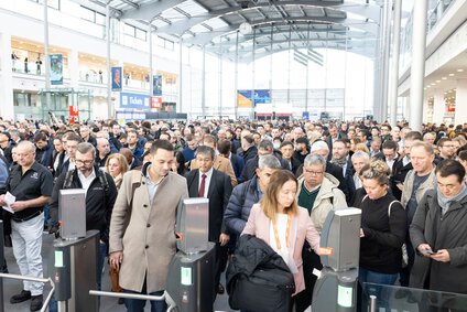 Numerous visitors stand in the entrance hall of the Munich Exhibition Centre, waiting to be admitted to the productronica trade fair.