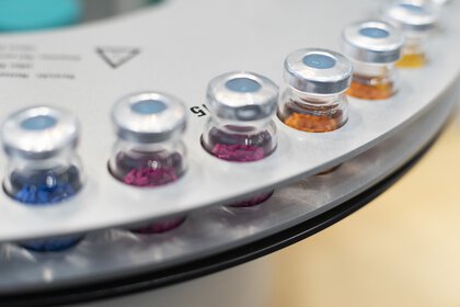 Close-up of an analyzer: Several vials with aluminum septum caps (vials) filled with colored grains are arranged in a circle in round holders.