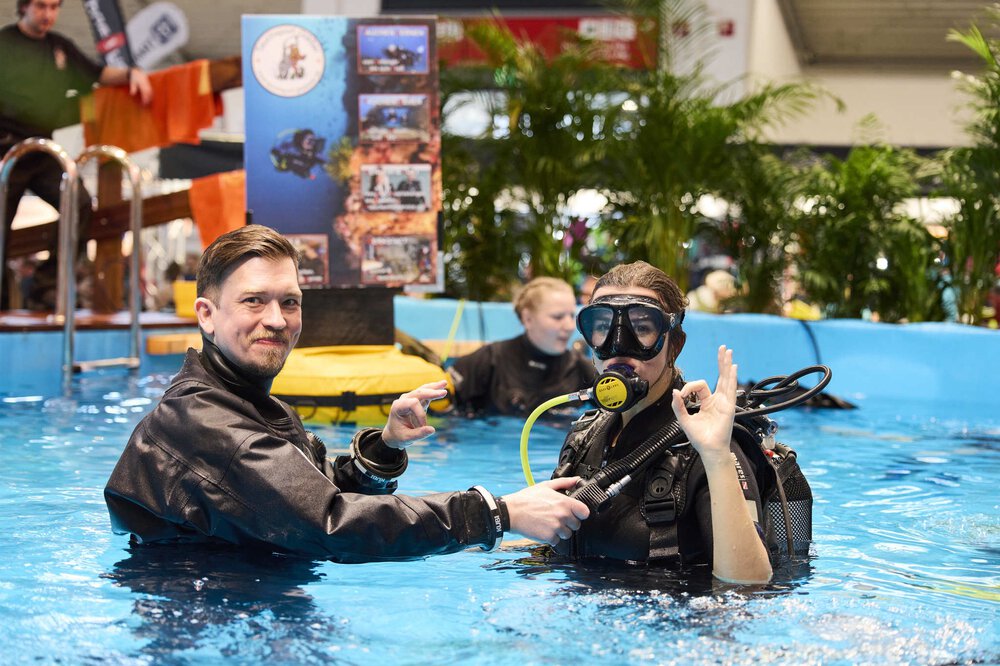 Three people in diving suits stand in a pool of water at the f.re.e exhibition.