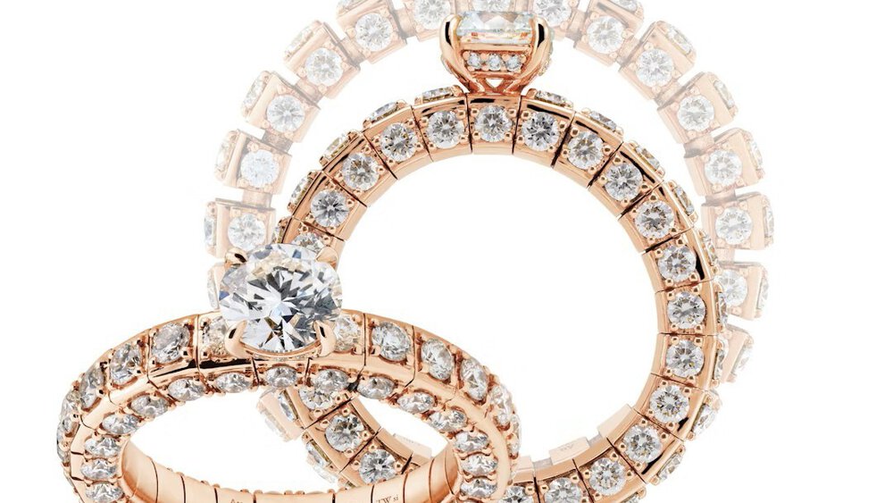 Three wide, multi-section rings set with numerous round diamonds and each featuring a large gemstone set on the side.