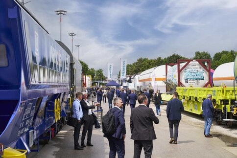 Visitors walk between containers and freight trains across the outdoor exhibition area.