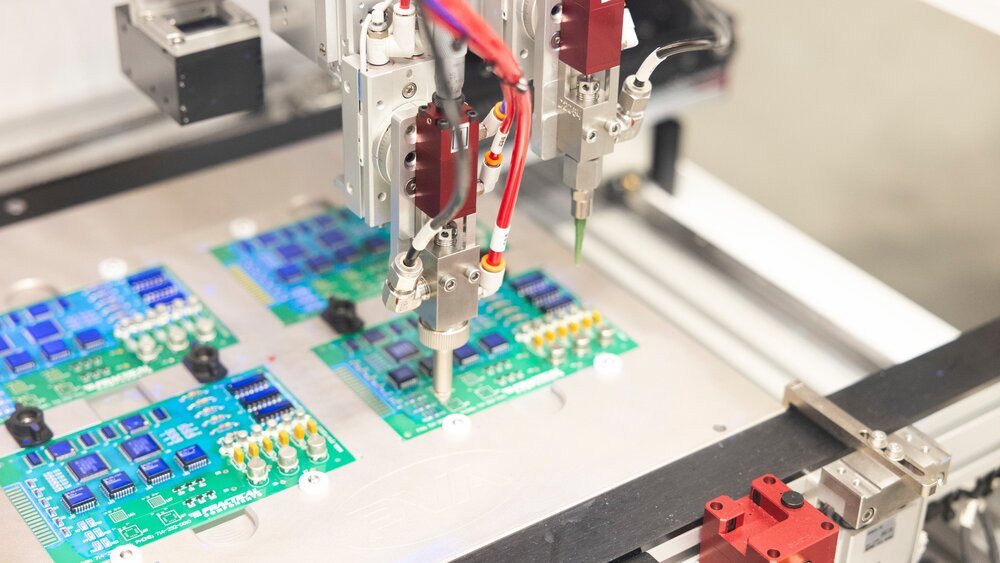 Nahansicht einer Maschine mit einem Präzessionswerkzeug an einem Roboterarm, welches über vier Leiterplatten schwebt.