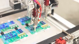 Nahansicht einer Maschine mit einem Präzessionswerkzeug an einem Roboterarm, welches über vier Leiterplatten schwebt.