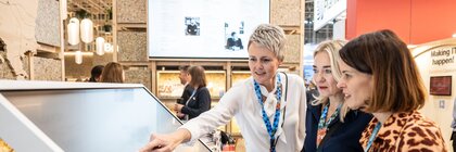 Eine Ausstellerin zeigt zwei Fachbesucherinnen Informationen auf einem Bildschirm