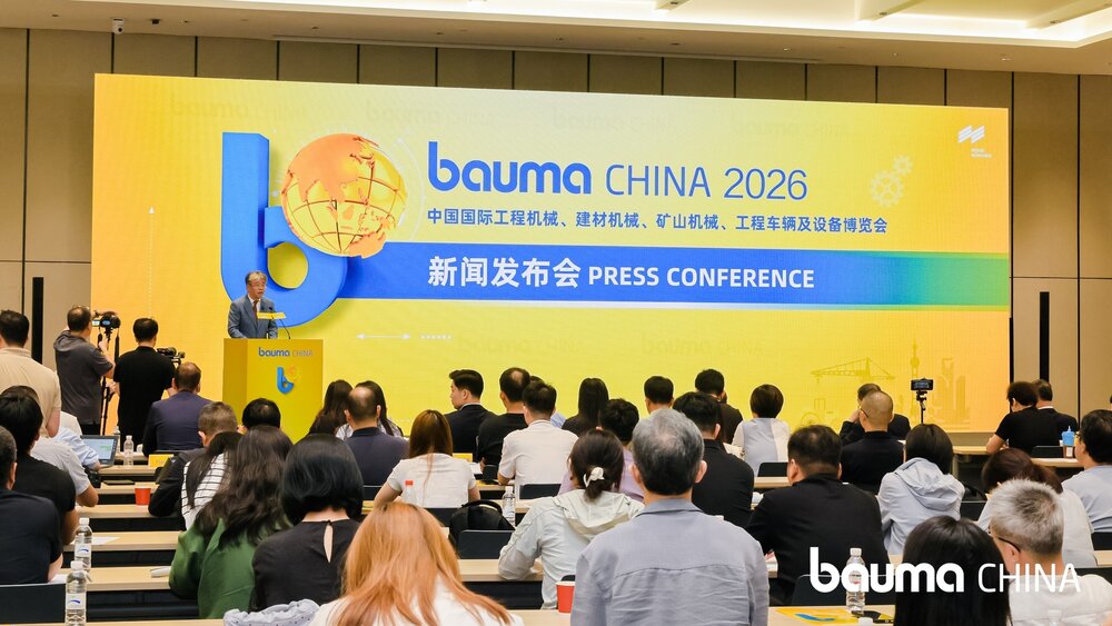 A press conference for bauma CHINA 2026, with participants seated and a speaker standing on the podium in front of a large yellow-and-blue event backdrop.