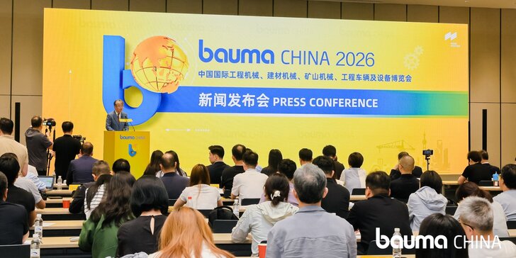 A press conference for bauma CHINA 2026, with participants seated and a speaker standing on the podium in front of a large yellow-and-blue event backdrop.