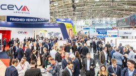 Zahlreiche Messebesucher stehen und gehen zwischen diversen farbenfrohen Messeständen der transport logistic Americas.