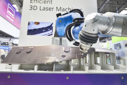 A robotic arm performs 3D laser processing of metal on an exhibit at a trade fair stand.