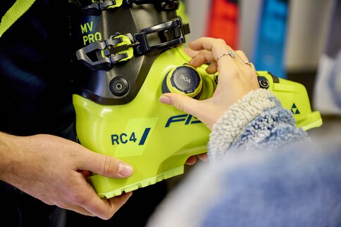 Eine Person dreht in einem Verkaufsraum an einen neongrünen Skischuh von Fischer mit RC4 an der Seite an dem BOA-Verschlusssystem, dass für einen sicheren und individuellen Sitz sorgt.