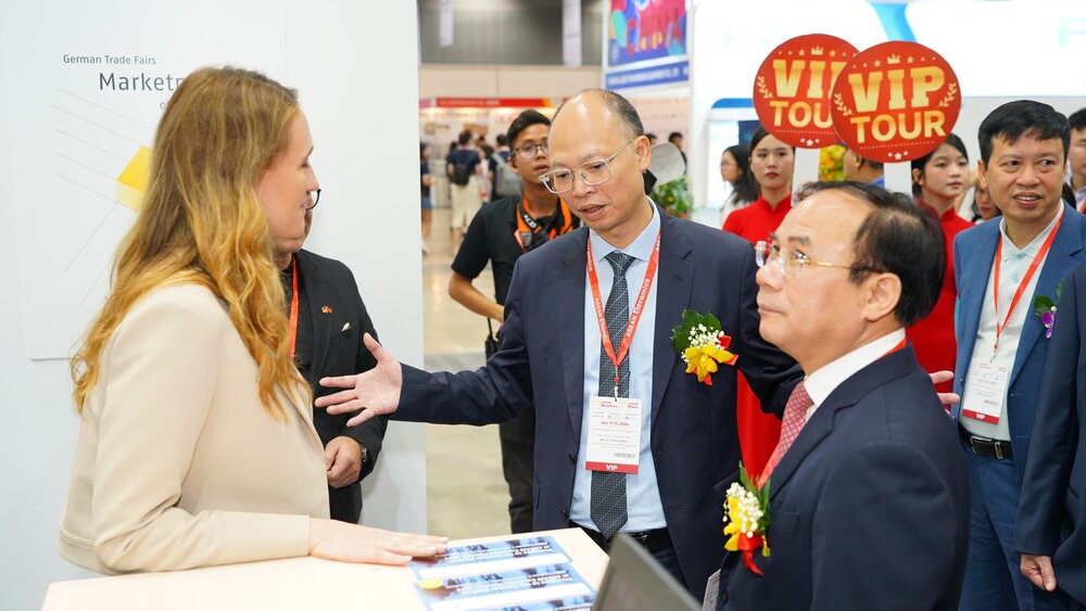 Several people in formal attire are standing together at a counter at an international ceramitec event, chatting.