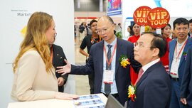 Several people in formal attire are standing together at a counter at an international ceramitec event, chatting.