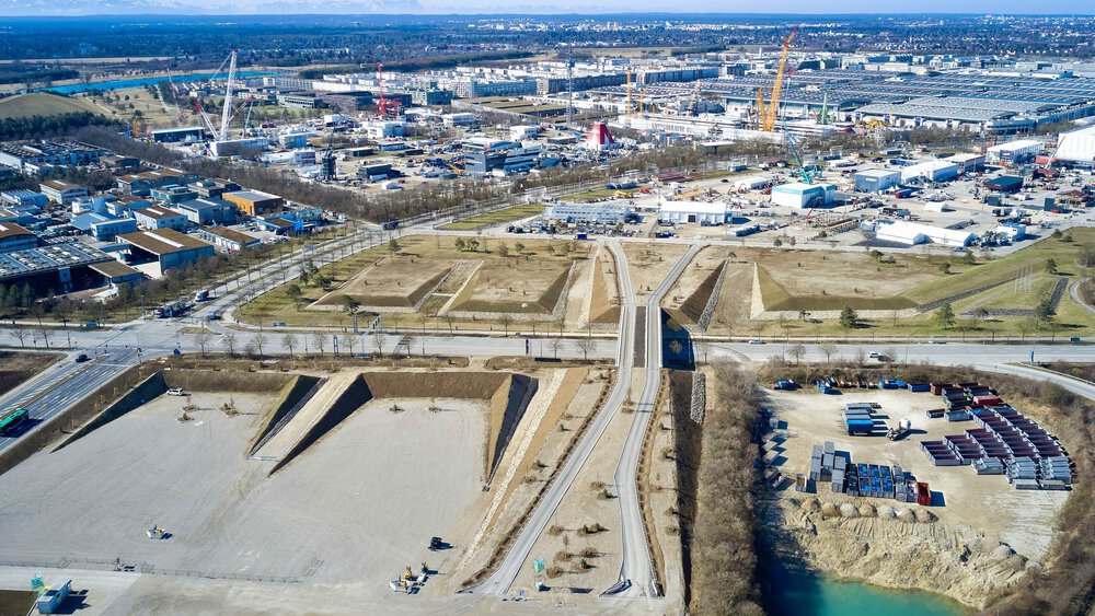 Aerial view of an industrial area with buildings, cranes, roads and a small turquoise body of water.