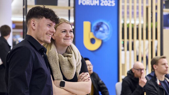 Two young trade fair visitors smiling in front of “bauma FORUM 2025” background.