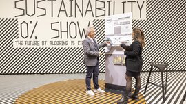 A presentation area with a black and white line pattern on the floor and wall. A man and a woman are standing in front of a display board and looking at carpet samples.