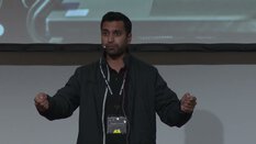 Ein Mann im schwarzen Sakko spricht gestikulierend vor einer Leinwand.