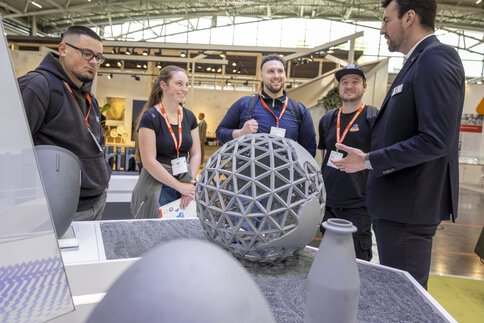 Five people talking about geometric ceramic products at an exhibition stand.