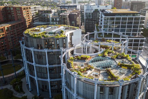 Vogelperspektive auf drei hohe runde Gebäude mit begrünten Dachterrassen und zahlreiche weitere Hochhäuser, die dahinter stehen.