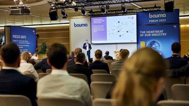 A speaker presents a slide to an audience in the Bauma Forum.