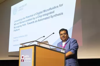 Anish Das der Universität Leipzig steht auf der analytica conference 2024 auf der Bühne hinter einem Pult und hält einen Vortrag. Im Hintergrund sieht man die Präsentation.