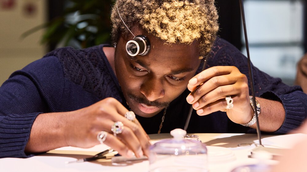A man examines small objects on a table with a magnifying glass, concentrating on his work.