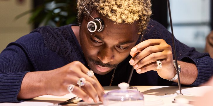 A man examines small objects on a table with a magnifying glass, concentrating on his work.