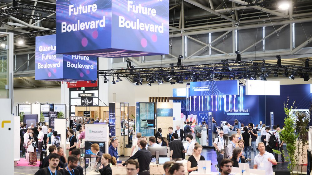 Blick über einen Teilbereich einer Messehalle mit zahlreichen Messeständen, an denen Aussteller und Besucher miteinander ins Gespräch kommen.
