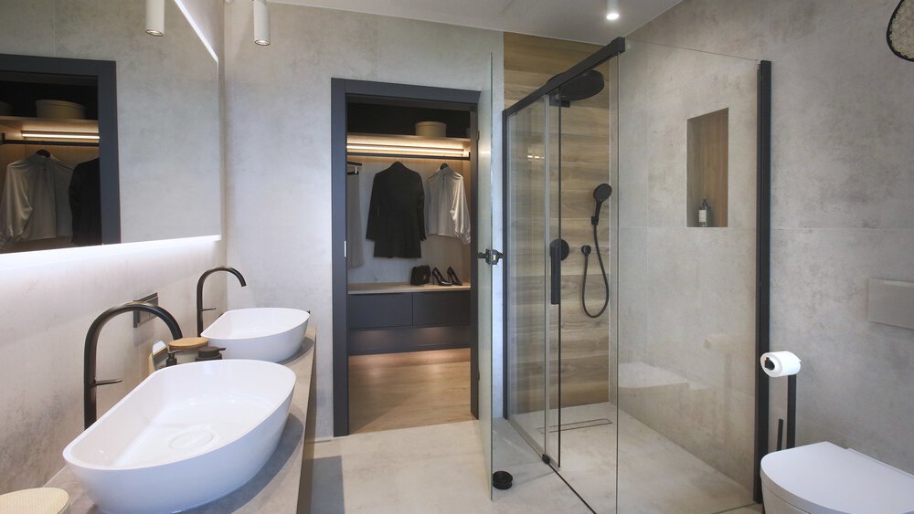 Modernes Badezimmer mit Glasdusche, Doppelwaschbecken und einer Glastür, die zu einem Schrank oder Ankleidezimmer führt.