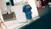 Service robot in blue clothing at an exhibition booth during DMEA