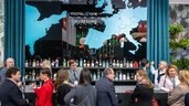 Trade fair visitors chat at a bar. A large map of Europe with the Motel One logo is emblazoned in the background.