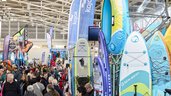 Exhibition stand at the f.re.e trade fair with colorful SUP boards, kayaks and water sports accessories, surrounded by many visitors.